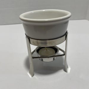 May include: White ceramic fondue pot with a silver metal stand and a small candle holder.