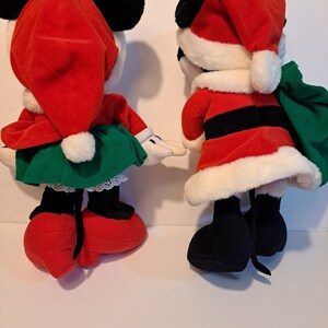 Puede incluir: Un par de juguetes de peluche de Mickey Mouse y Minnie Mouse con tem&aacute;tica navide&ntilde;a. Mickey est&aacute; vestido de Pap&aacute; Noel con un traje rojo, cintur&oacute;n negro y ribetes blancos. Minnie lleva un gorro de Pap&aacute; Noel rojo, un vestido verde y zapatos blancos.