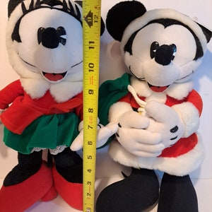Puede incluir: Un par de juguetes de peluche de Mickey Mouse y Minnie Mouse con tem&aacute;tica navide&ntilde;a. Mickey lleva un traje de Pap&aacute; Noel rojo y blanco con una bolsa verde. Minnie lleva un vestido rojo y blanco con una falda verde y un ribete de encaje blanco. Ambos juguetes miden aproximadamente 30 cm de alto.
