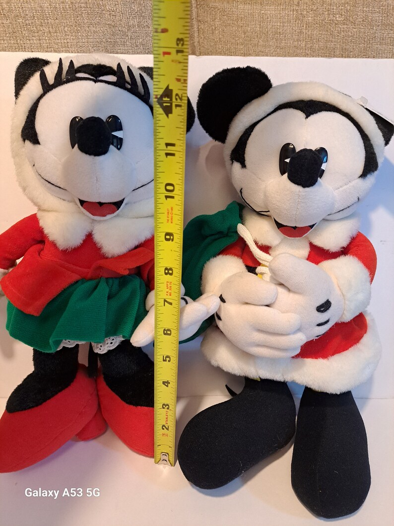 Puede incluir: Un par de juguetes de peluche de Mickey Mouse y Minnie Mouse con tem&aacute;tica navide&ntilde;a. Mickey lleva un traje de Pap&aacute; Noel rojo y blanco con una bolsa verde. Minnie lleva un vestido rojo y blanco con una falda verde y un ribete de encaje blanco. Ambos juguetes miden aproximadamente 30 cm de alto.