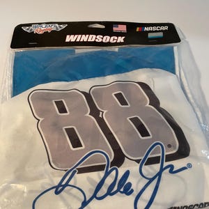 May include: A white windsock with the number "88" in grey with a black outline, and a blue signature. The packaging top reads "Wincraft Racing" and "Windsock". The packaging also includes the text "Proudly Made" and the NASCAR logo.