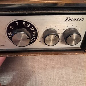 Pu&ograve; includere: Primo piano di un giradischi Emerson vintage con una piastra frontale argentata e tre manopole. Le manopole sono etichettate "off", "low" e "tone". Il giradischi ha una finitura in legno di colore marrone e nero.