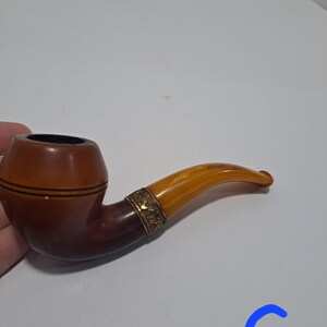 Op de afbeelding: Een bruine en amberkleurige pijp met een gouden band. De pijp heeft een gebogen steel en een kom met een bruin en amberkleurig patroon.