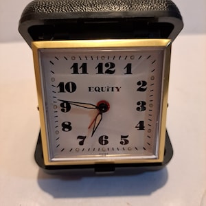 May include: A gold-colored alarm clock with a white face and black numbers. The clock is in a black case and has the word "EQUITY" printed on the face.