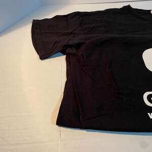 May include: A black short-sleeved t-shirt featuring a large white graphic print on the front. The design includes a partial white shape at the top and the white capital letters G and V visible near the bottom edge of the fabric.