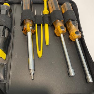 May include: A black zippered case with a set of screwdrivers and a pair of tweezers. The screwdrivers have yellow and brown handles and the tweezers are yellow.