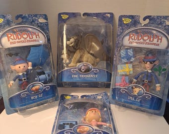 May include: Four plastic packages containing action figures from the Rudolph the Red-Nosed Reindeer movie. The figures include Boy Elf, Tall Elf, Girl Elf, and King Moonracer.