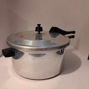 May include: A silver aluminum pressure cooker with a black handle and a red pressure release valve.