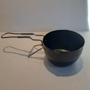 May include: A black metal camping pot with a foldable handle. The pot is round and has a smooth surface.