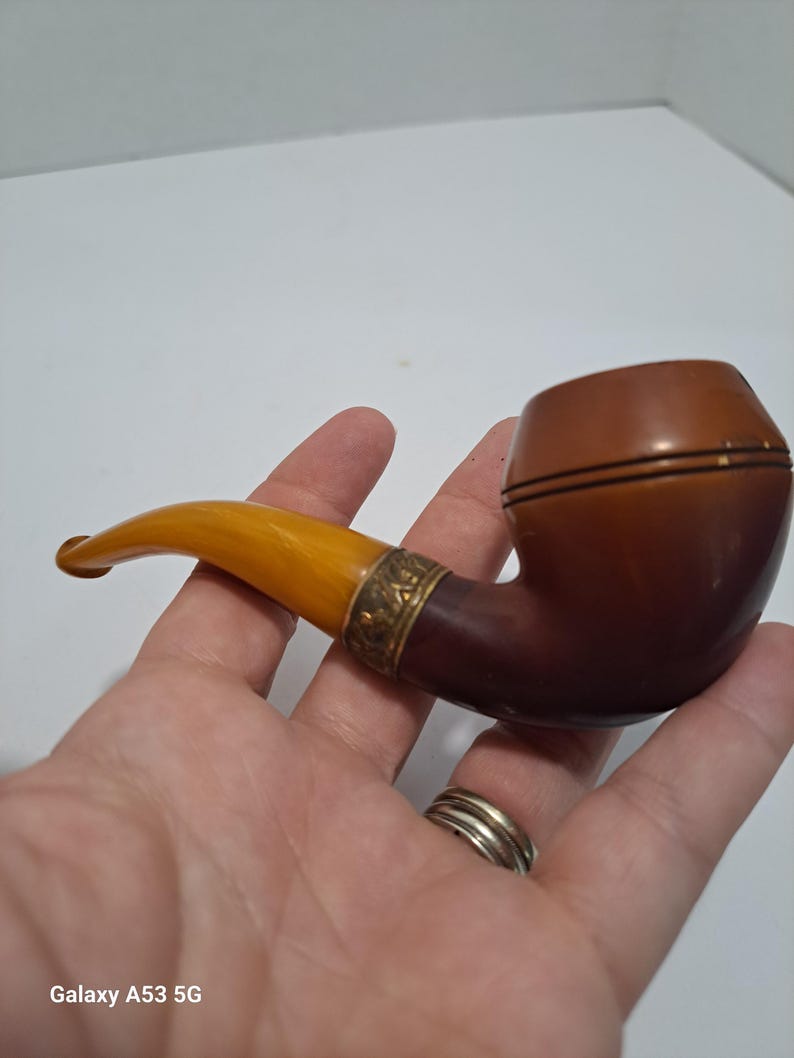 Op de afbeelding: Een bruine en amberkleurige pijp met een gouden band. De pijp wordt in een hand gehouden.