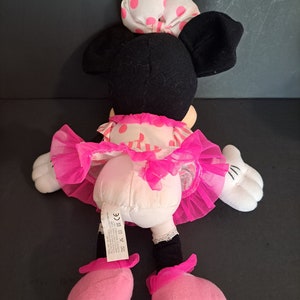 May include: Pink and black plush Minnie Mouse toy wearing a pink polka dot dress and a white bow with pink polka dots. The toy has a pink tulle skirt and pink shoes.