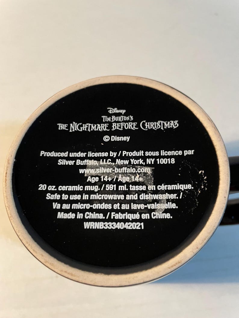 May include: A black ceramic mug base featuring white text that reads Disney Tim Burton's The Nightmare Before Christmas, Silver Buffalo, LLC, New York, NY 10018, 20 oz. ceramic mug, safe to use in microwave and dishwasher, Made in China, WRNB3334042021.