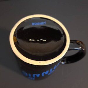 Peut inclure: Mug en c&eacute;ramique noire avec un bord blanc et une anse. Le mug pr&eacute;sente un texte bleu qui dit "Minnie". Le fond du mug porte l'inscription "&copy;DISNEY" et "Made in China".
