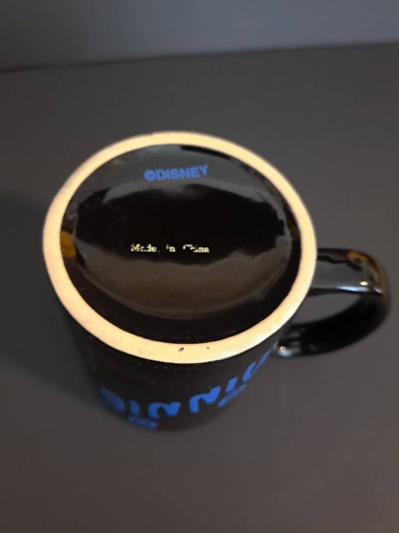 Peut inclure: Mug en c&eacute;ramique noire avec un bord blanc et une anse. Le mug pr&eacute;sente un texte bleu qui dit "Minnie". Le fond du mug porte l'inscription "&copy;DISNEY" et "Made in China".