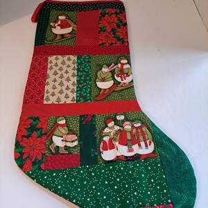 May include: A red and green Christmas stocking with a patchwork design featuring snowmen, poinsettias, and evergreen trees.
