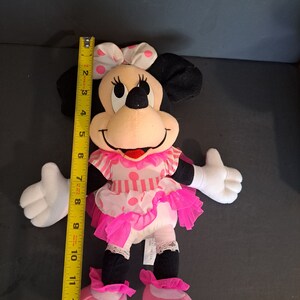 May include: Pink and black plush Minnie Mouse doll wearing a pink and white polka dot dress with a pink bow. The doll is approximately 12 inches tall.