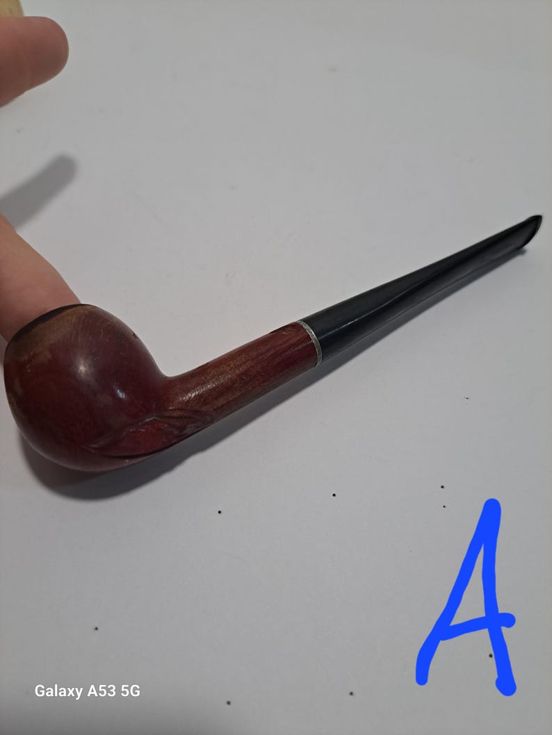 Op de afbeelding: Een bruine houten pijp met een zwarte steel. De pijp heeft een gesneden ontwerp op de kom.