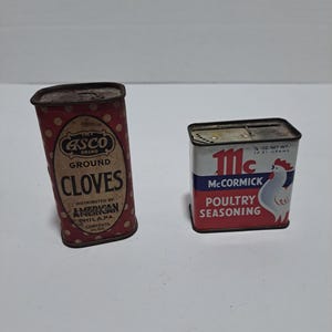 Peut inclure: Deux boîtes d'épices vintage. La boîte de gauche est rouge avec des pois blancs et indique "ASCO BRAND GROUND CLOVES" et "DISTRIBUTED BY AMERICAN PHILA.PA. CONTENTS 1/2 OZ". La boîte de droite est blanche avec des accents rouges et bleus et indique "111c McCORMICK POULTRY SEASONING" et "1/2 OZ NET WT. 14.21 GRAMS".