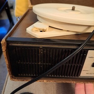 Pu&ograve; includere: Un giradischi vintage marrone e nero con un piatto girevole bianco. Il giradischi ha un selettore radio e phono.