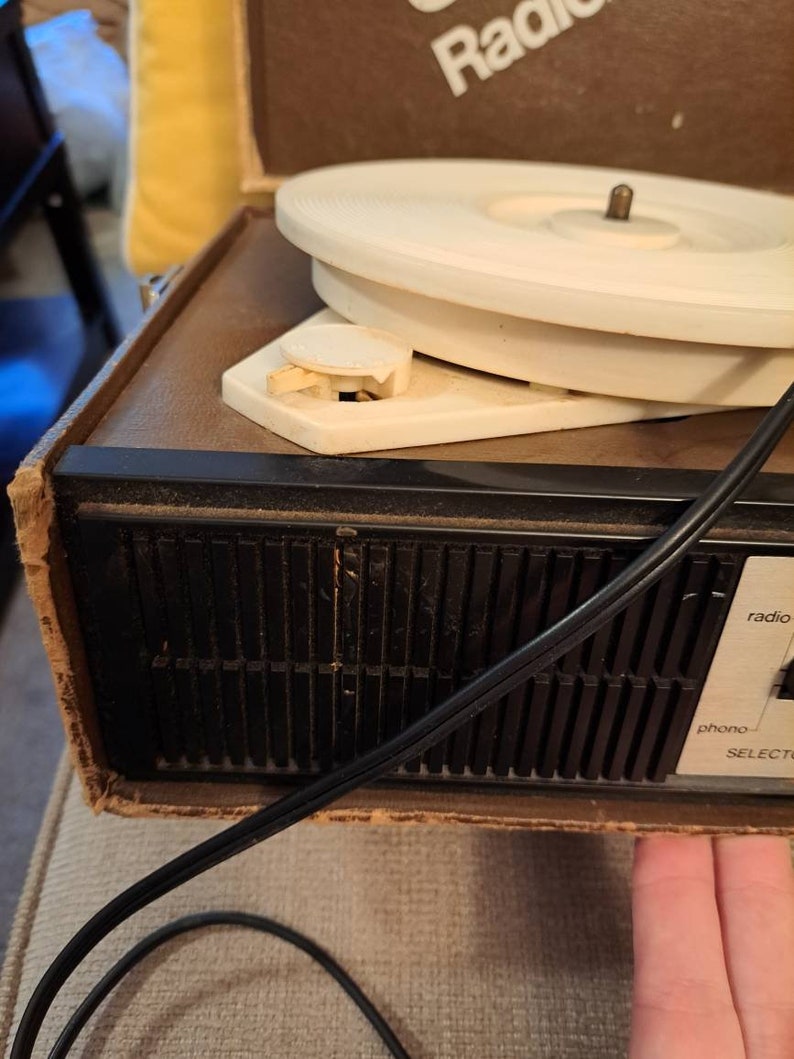 Pu&ograve; includere: Un giradischi vintage marrone e nero con un piatto girevole bianco. Il giradischi ha un selettore radio e phono.