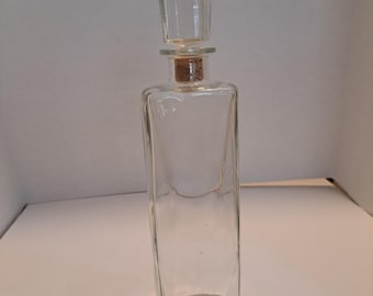 May include: A clear glass decanter with a square body and a square stopper. The stopper is made of cork.