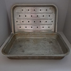 May include: A silver metal baking pan with a removable rack. The pan has a rectangular shape and is slightly worn. The rack has a grid pattern with holes for air circulation.