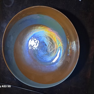 May include: A large, brown ceramic bowl with a swirling blue and iridescent glaze. The bowl has a wide rim and a deep, rounded interior.