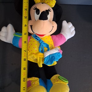 May include: A plush Minnie Mouse toy wearing a yellow dress with pink polka dots, a blue purse, and yellow shoes with pink polka dots. The toy has black ears and a red bow.