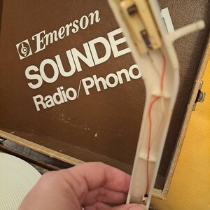 Pu&ograve; includere: Primo piano di un braccio di un giradischi bianco con un filo rosso che lo attraversa. Il braccio &egrave; attaccato a un giradischi vintage Emerson Sounde Radio/Phono.
