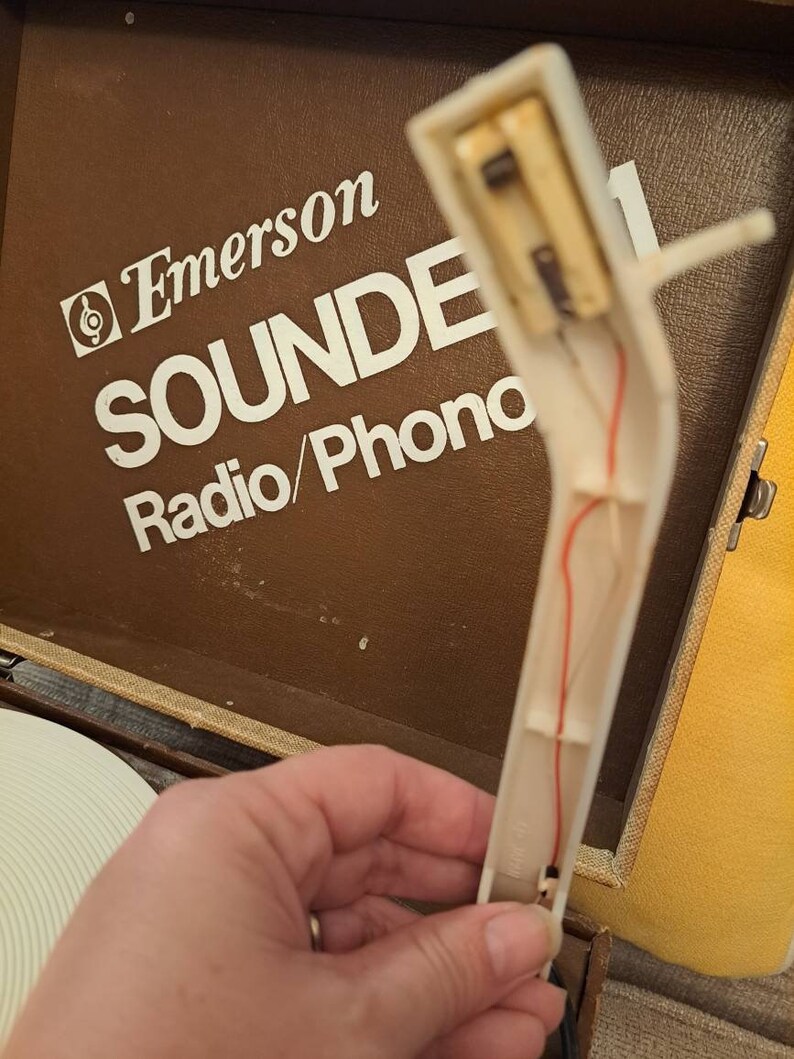 Pu&ograve; includere: Primo piano di un braccio di un giradischi bianco con un filo rosso che lo attraversa. Il braccio &egrave; attaccato a un giradischi vintage Emerson Sounde Radio/Phono.