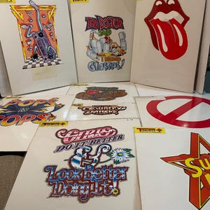 May include: A collection of vintage graphic t-shirts featuring various designs. The shirts showcase bold graphics, including a musical instrument, a doctor with glasses, a red tongue, and the text "Girls Do It Better & Look Better Doing It!"