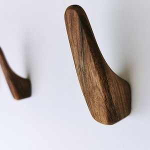 May include: Four wooden wall hooks in a row, each with a curved design. The hooks are made of dark brown wood with a natural grain pattern.