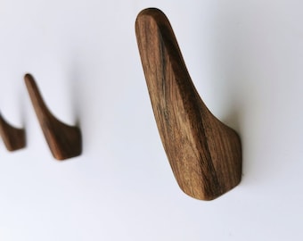 May include: Four wooden wall hooks in a row, each with a curved design. The hooks are made of dark brown wood with a natural grain pattern.