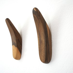 Könnte beinhalten: Zwei Wandhaken aus Holz mit einem geschwungenen Design. Die Haken sind aus dunklem Holz mit einer helleren Holzveredelung am Boden.