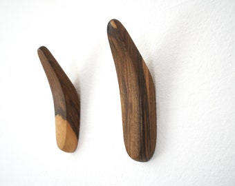 May include: Two wooden wall hooks with a curved design. The hooks are made of dark wood with a lighter wood finish on the bottom.