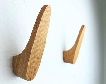 May include: Two wooden wall hooks in the shape of a curved blade. The hooks are made of light brown wood and are mounted on a white wall.