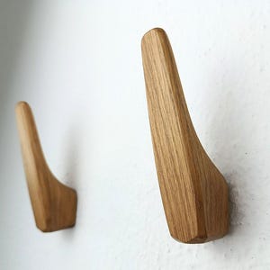 Pode incluir: Dois ganchos de parede de madeira com um design curvo. Os ganchos são feitos de madeira marrom claro e têm um acabamento liso.