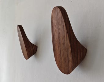 May include: Two wooden wall hooks with a curved design. The hooks are made of dark brown wood and are mounted on a white wall. The hooks are designed to hold coats, hats, or other items.
