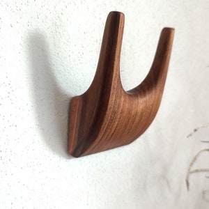 Könnte beinhalten: Ein Wandhaken aus Holz mit einem einzigartigen, geschwungenen Design. Der Haken ist aus dunkelbraunem Holz gefertigt und hat eine glatte Oberfläche.