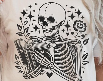May include: A black and white illustration of a skeleton reading a book with a heart and flowers around it. The skeleton is wearing a shirt with a skull on it.