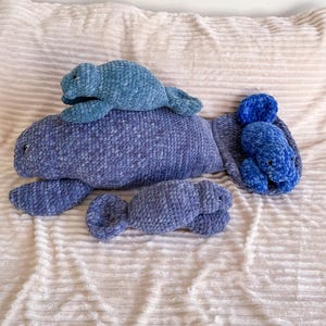 Puede incluir: Tres juguetes de peluche de manat&iacute; de crochet en tonos azules. El manat&iacute; m&aacute;s grande est&aacute; acostado con la cola enroscada. Un manat&iacute; m&aacute;s peque&ntilde;o est&aacute; acostado encima del m&aacute;s grande. El manat&iacute; m&aacute;s peque&ntilde;o est&aacute; acostado de lado con la cola enroscada.