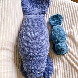 Puede incluir: Dos peluches de manat&iacute; de crochet. El manat&iacute; m&aacute;s grande es azul y el m&aacute;s peque&ntilde;o es azul verdoso. Ambos manat&iacute;es est&aacute;n acostados sobre una manta blanca y esponjosa.