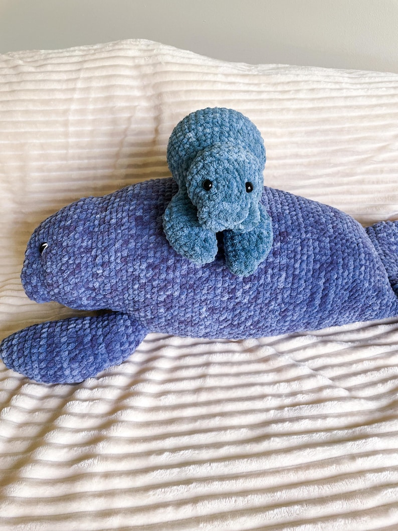Puede incluir: Un juguete de peluche de manat&iacute; de crochet azul con un juguete de peluche de tortuga de crochet azul m&aacute;s peque&ntilde;o encima. Ambos juguetes est&aacute;n sentados en una manta blanca y esponjosa.