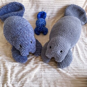 Puede incluir: Tres peluches de manat&iacute; de crochet en tonos azules. El manat&iacute; m&aacute;s grande est&aacute; acostado, mientras que el m&aacute;s peque&ntilde;o est&aacute; sentado. El manat&iacute; m&aacute;s peque&ntilde;o es un beb&eacute; manat&iacute;.