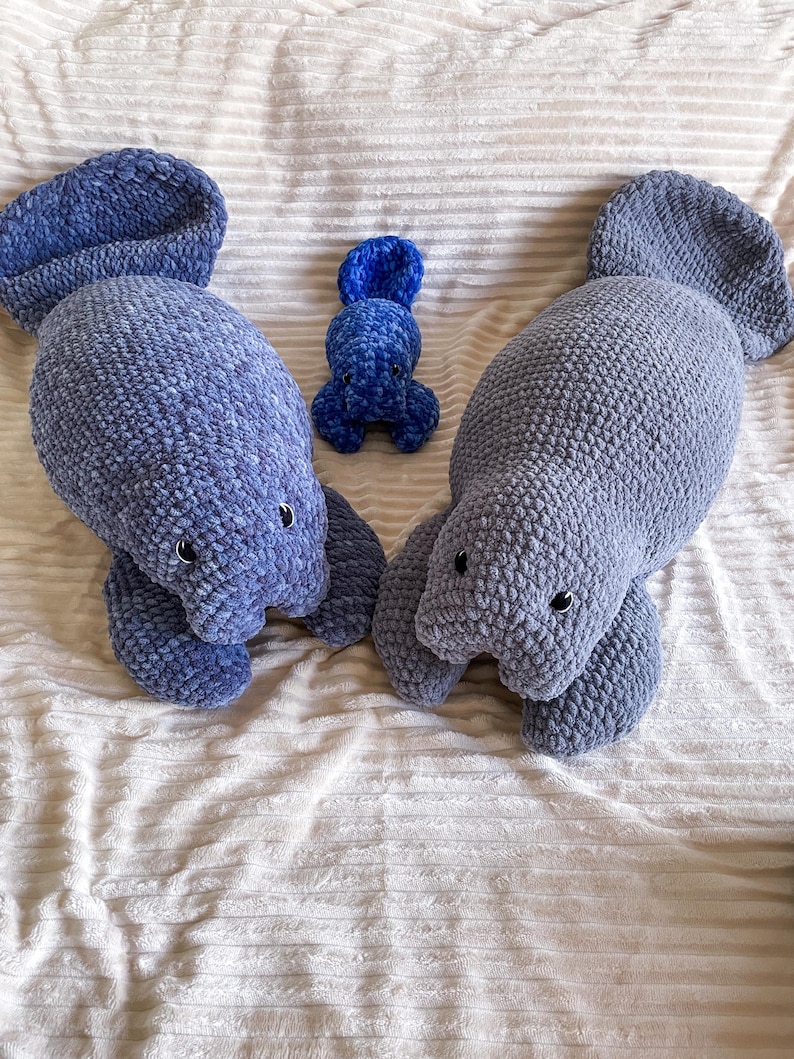 Puede incluir: Tres peluches de manat&iacute; de crochet en tonos azules. El manat&iacute; m&aacute;s grande est&aacute; acostado, mientras que el m&aacute;s peque&ntilde;o est&aacute; sentado. El manat&iacute; m&aacute;s peque&ntilde;o es un beb&eacute; manat&iacute;.