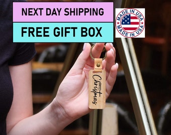 May include: A wooden keychain with a brown leather strap and a gold metal ring. The keychain has the text "merry Christmas" engraved on it.