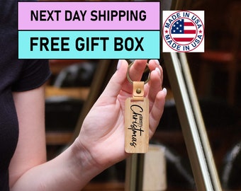 May include: A wooden keychain with a brown leather strap and a gold metal ring. The keychain has the words "merry Christmas" engraved on it.
