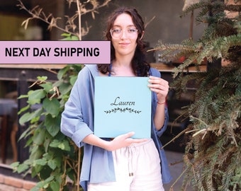 May include: A light blue personalized notebook with the name "Lauren" written in black script on the front cover. The notebook is decorated with a simple floral design.