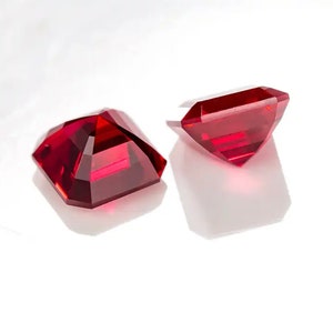 May include: Two red gemstone, square-shaped, cut gems on a white background.