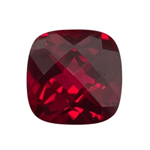 May include: A deep red cushion-cut gemstone with a faceted surface.